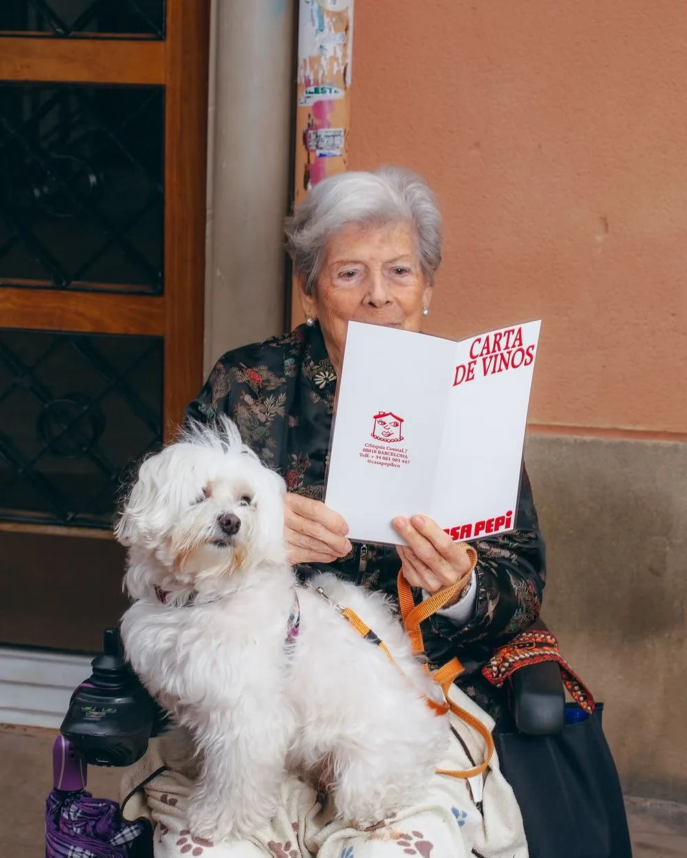 Una clienta sentada a la puerta de Casa Pepi, con su perro en el regazo, leyendo la carta de vinos del restaurante