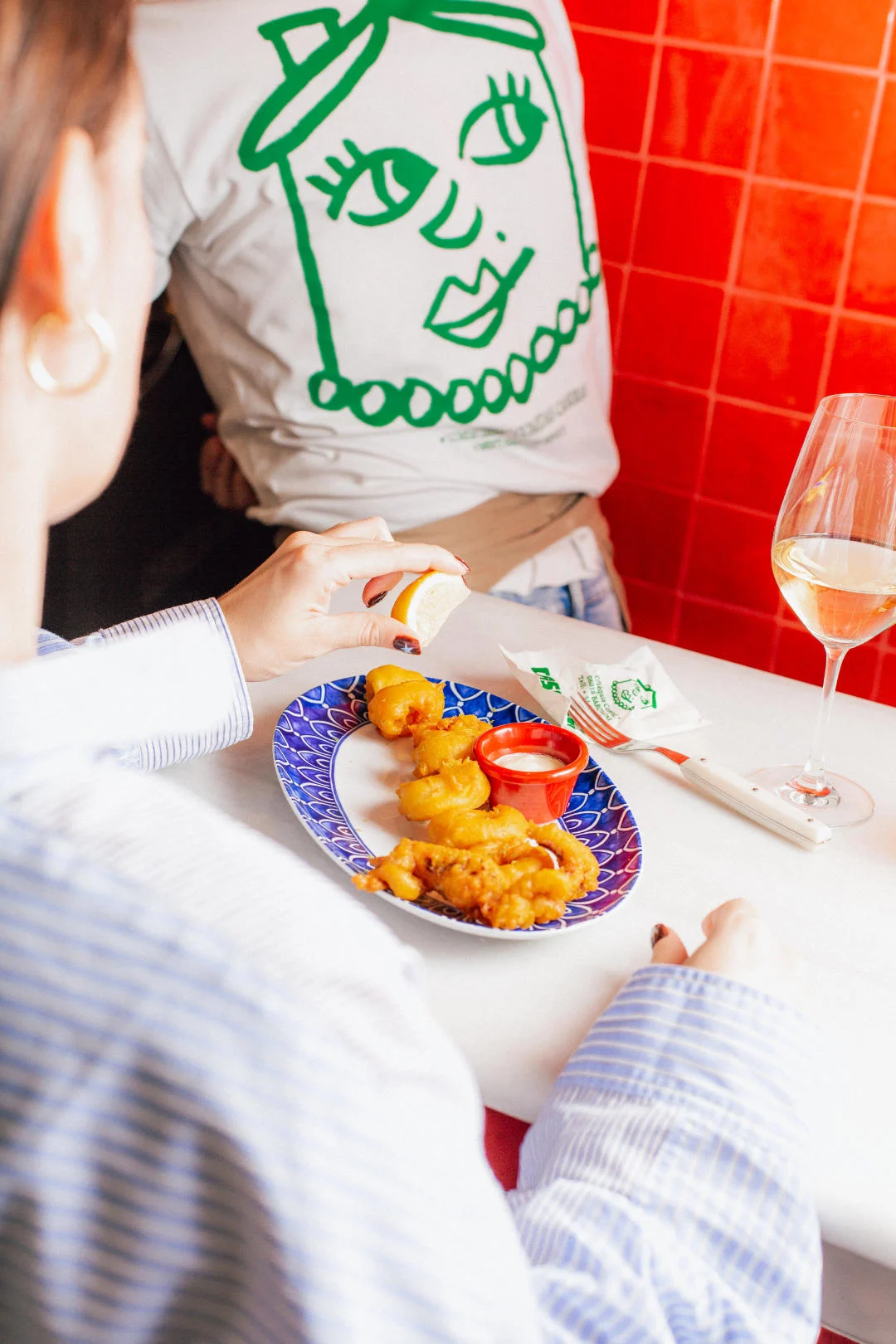 Persona comiendo gambas rebozadas, con copa de vino en la mesa