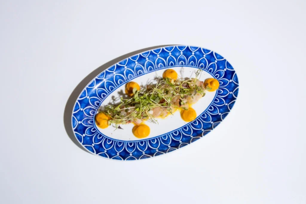 Plato de ceviche con salsas y brotes verdes en un plato azul en Casa Pepi